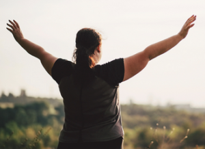 Woman holding her arms up and looking out over a field.
