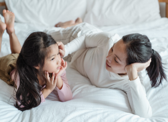 Women and daughter laying on bed talking to each other.