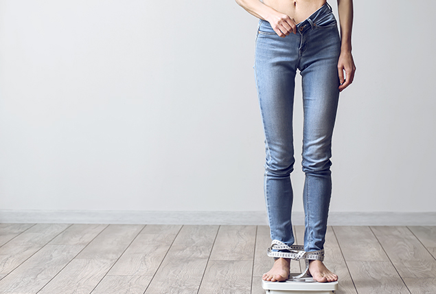 A person stands in jeans with measuring tape around their ankles.