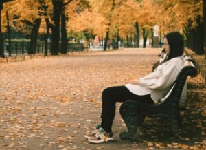 A woman sitting on a park bench in autumn, reflecting on the emotional shifts that can come with Seasonal Affective Disorder.